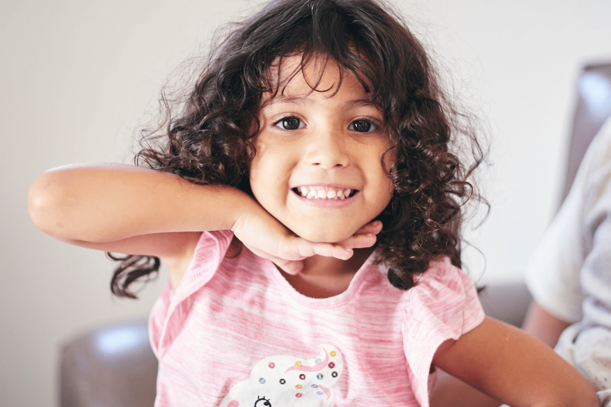 a little girl smiling and putting a hand underneath her chin