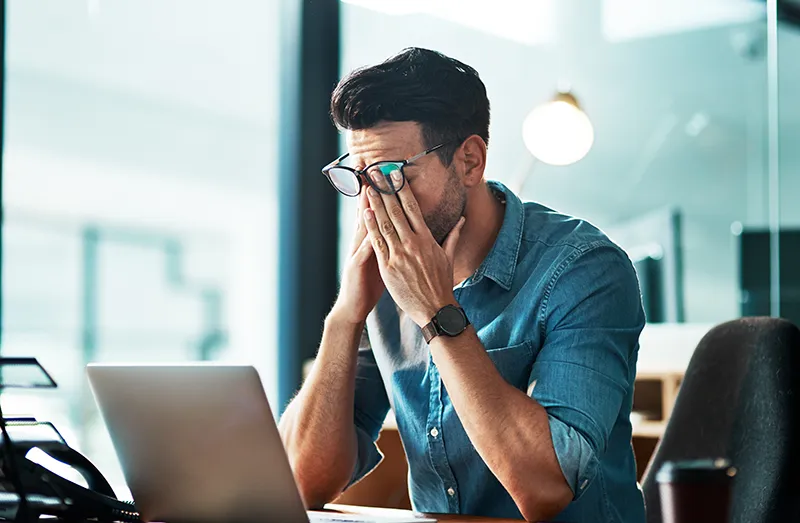 a man sitting at his desk at work and rubbing his eyes