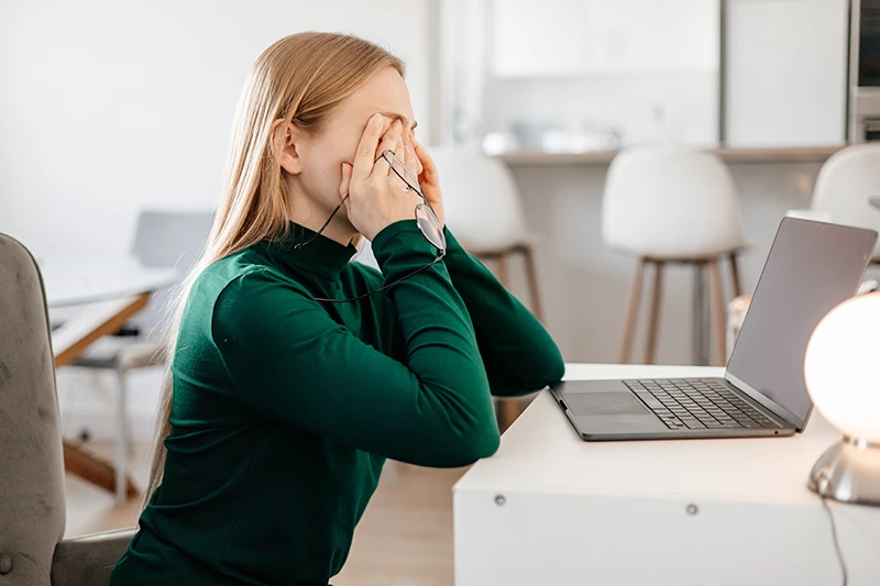 a woman sitting at a desk rubbing her eyes due to eye strain