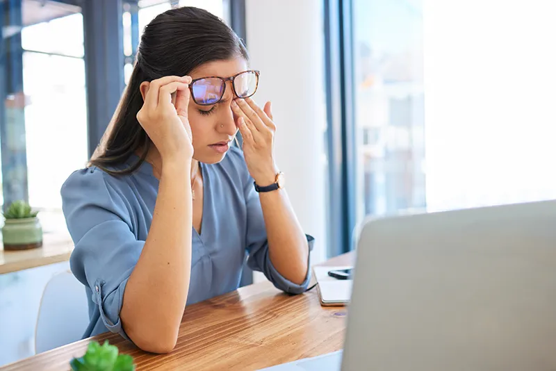 a woman sitting in front of her computer at work and rubbing her eye