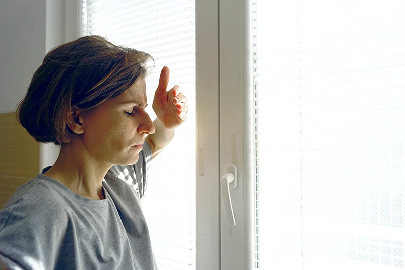 light-sensitivity-headaches a woman shielding her eyes from window light due to photophobia