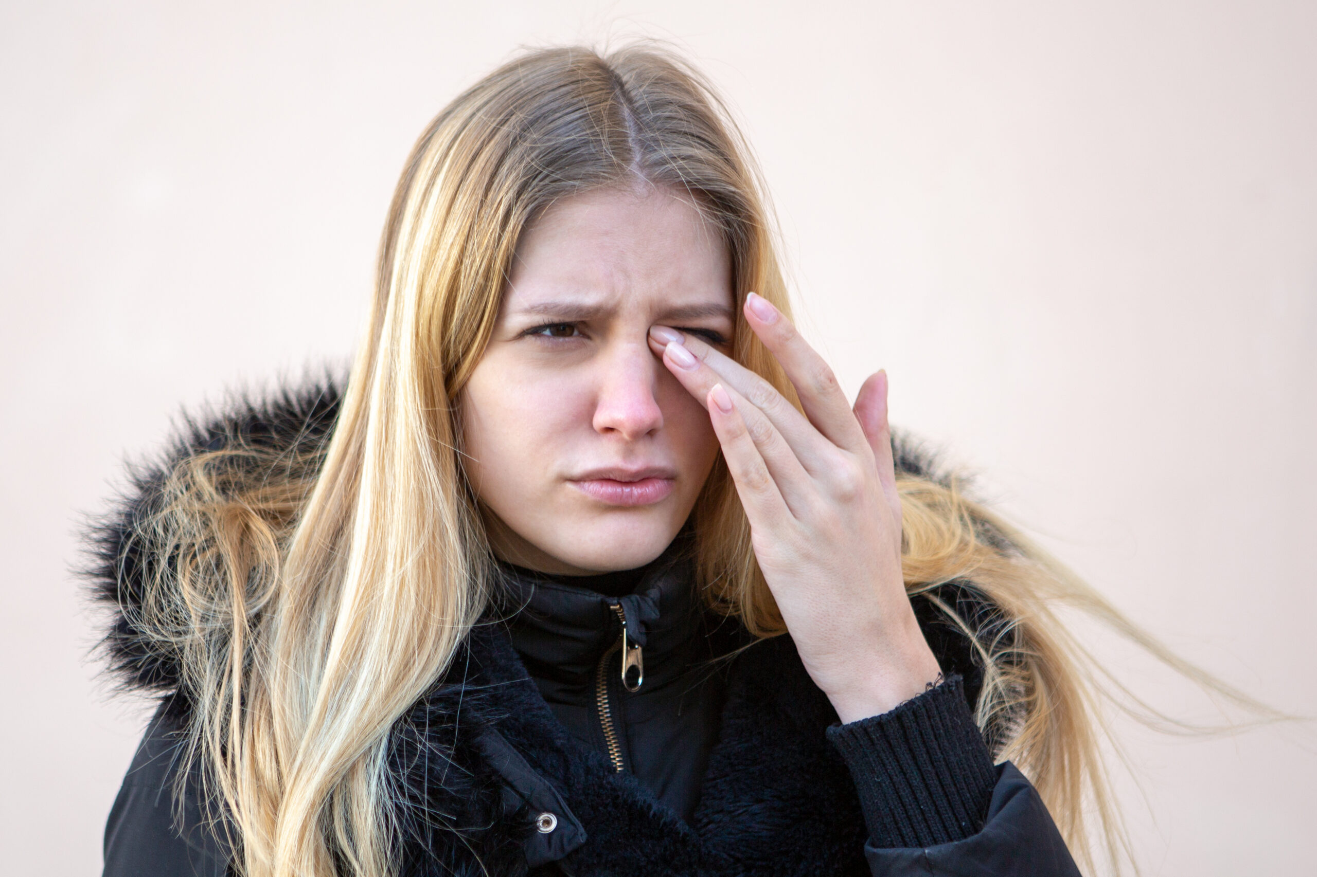 A woman wearing a coat rubs her irritated eye.